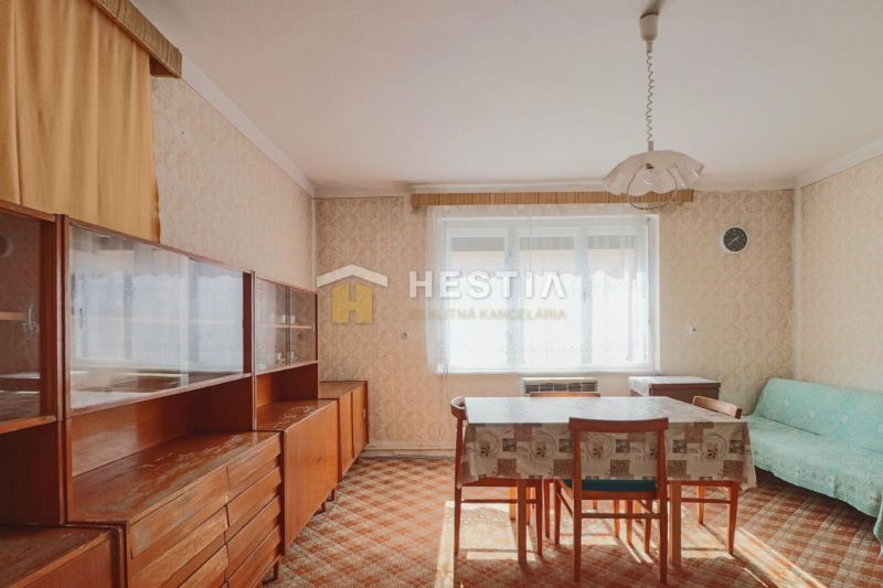 Étkező egy családi házban retro bútorokkal és szőnyeggel, dominál egy világos ablak.