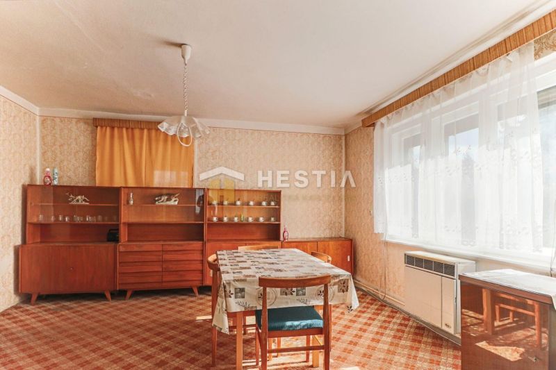 Családi ház belső tere étkezőasztallal, régebbi bútorokkal és szőnyeggel.