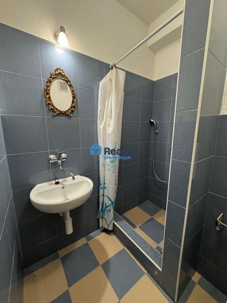 Fürdőszoba egy kétszobás lakásban mosdóval, tükörrel és zuhanyzóval, kék csempékkel.