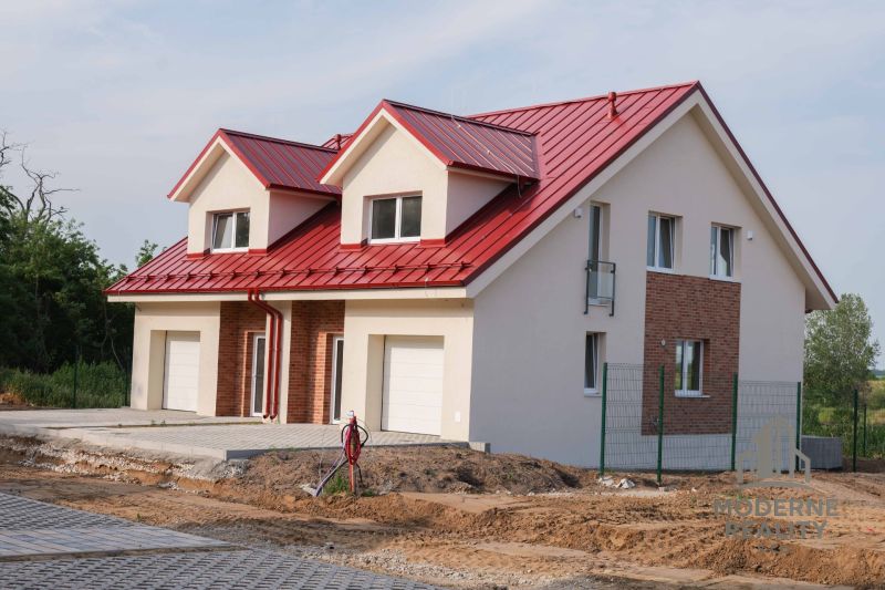 Családi ház Andócon piros tetővel és fehér garázskapukkal.
