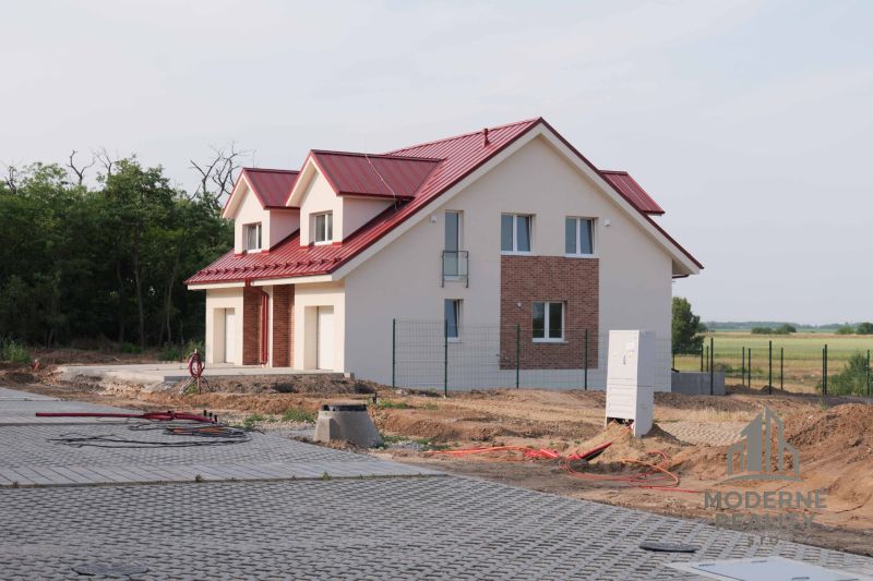 Családi ház Andódon piros tetővel, fákkal körülvéve és rendezett felhajtóval.