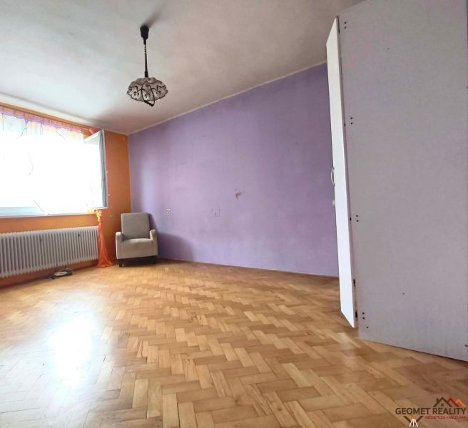 Nappali egy háromszobás lakásban, fa dekoros padlóval és lila fallal.