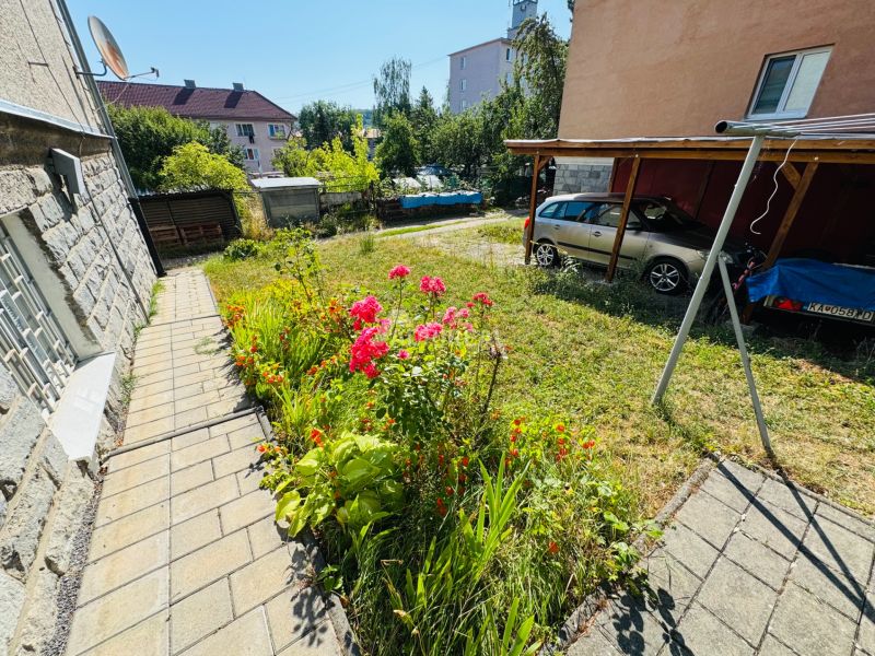 Virágágyások az út mellett Krupinában, a 2 szobás lakás mellett, autó a tető alatt parkolva.