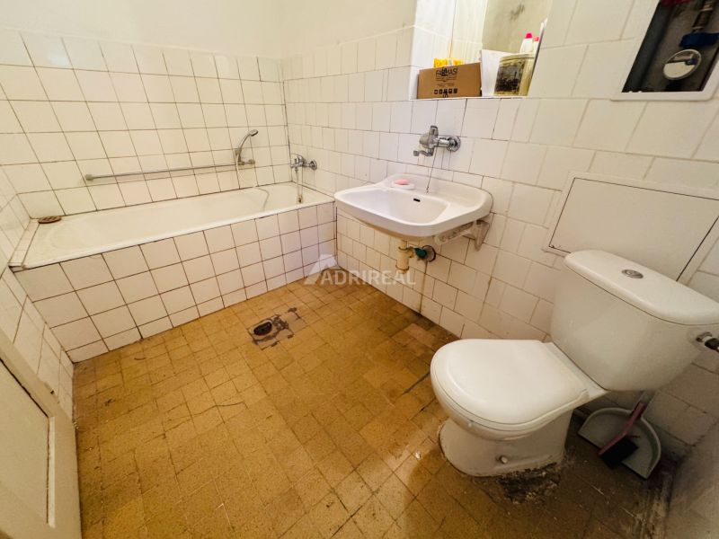 Fürdőszoba egy kétszobás lakásban káddal, mosdóval és WC-vel, fehér csempével burkolva.