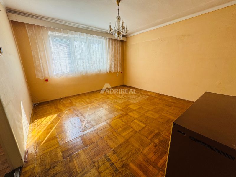 Szoba egy kétszobás lakásban kristálycsillárral és fa dekorációjú padlóval.