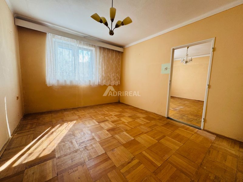 Szoba egy kétszobás lakásban, fa dekorációjú padlóval és függönyökkel az ablakon.
