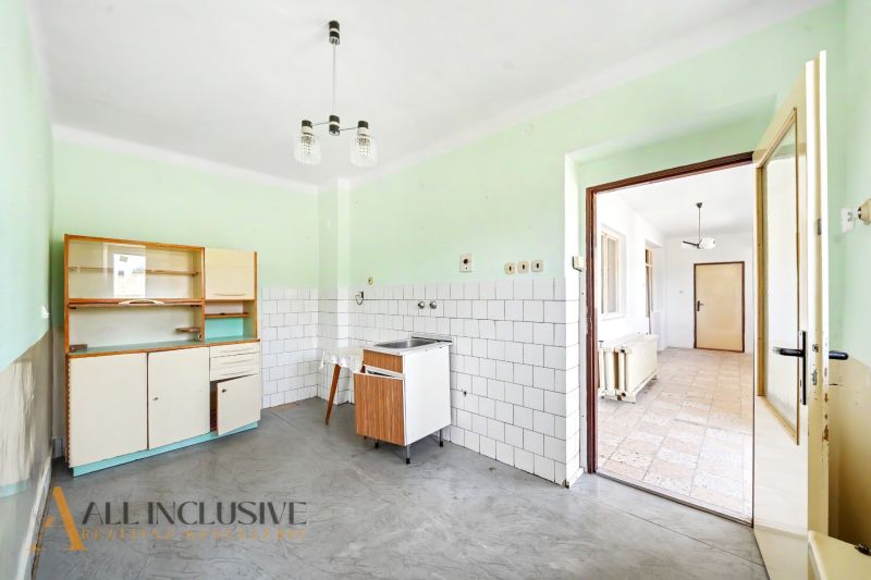Konyha egy családi házban egyszerű konyhabútorral, fehér csempékkel és szürke padlóval.