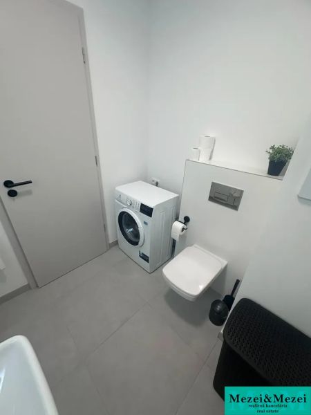 Fürdőszoba mosógéppel, WC-vel és bézs csempével egy kétszobás lakásban.