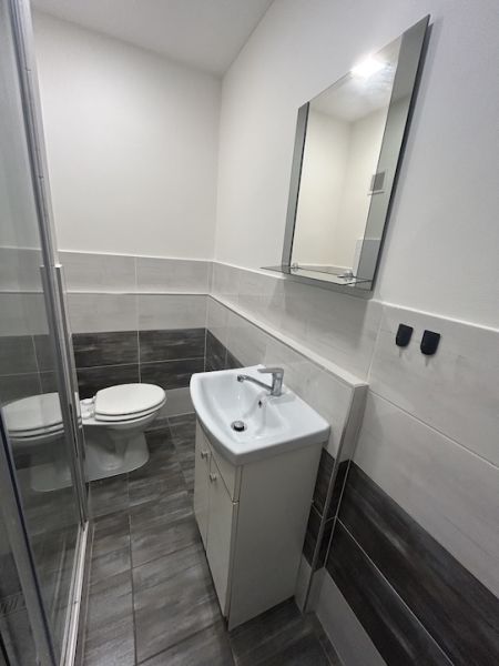 Fürdőszoba garzonlakásban WC-vel, mosdóval és zuhanyzóval, semleges színárnyalatokkal.