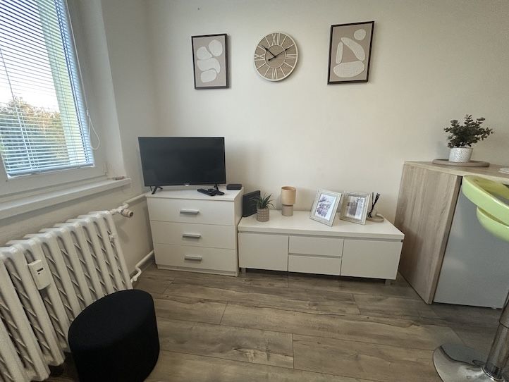 Garzonlakás fa hatású padlóval, fehér bútorokkal és faldekorációkkal.