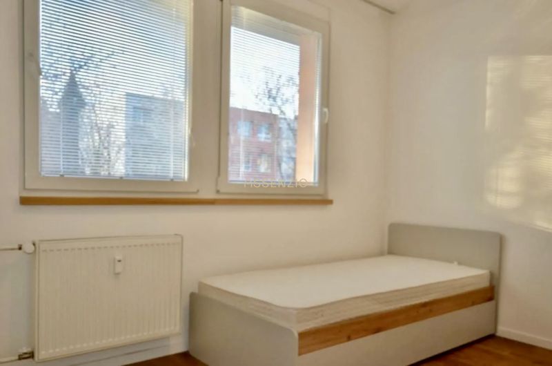 Hálószoba egy háromszobás lakásban nagy ablakokkal és fa dekorációjú padlóval.