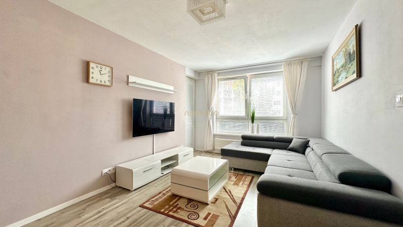 Nappali sarokkanapéval, TV-vel, dohányzóasztallal és fa mintázatú padlóval.