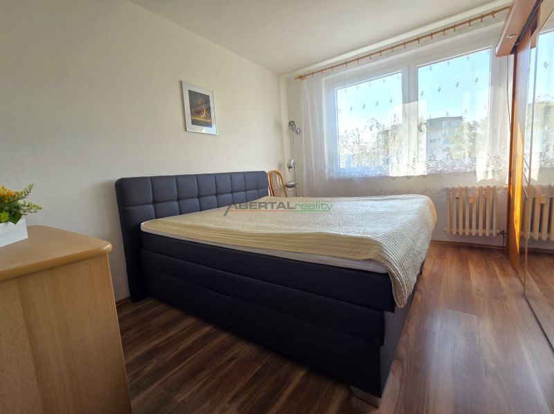 Hálószoba nagy ággyal, fa dekorációjú padlóval és ablakkal egy háromszobás lakásban.
