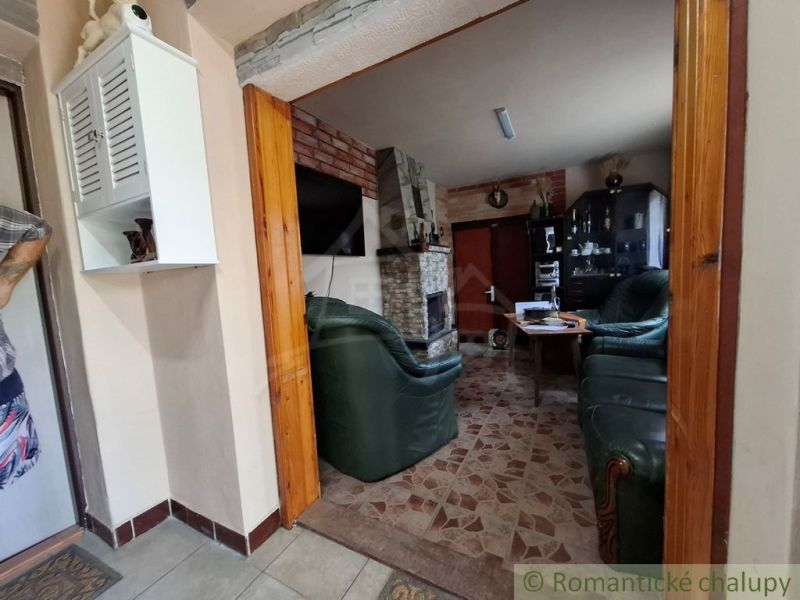 Nappali egy faházban kandallóval, bőr ülőgarnitúrával és fehér szekrénnyel.