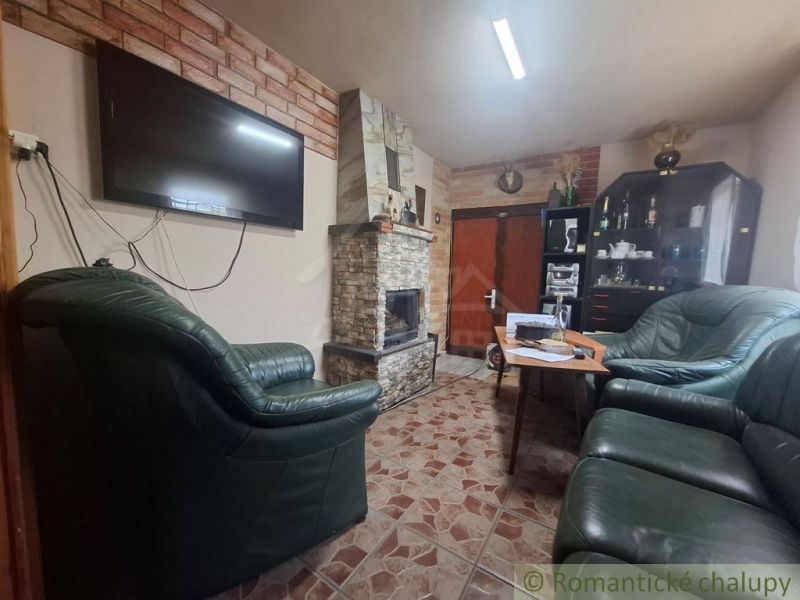 Kő kandalló és bőr kanapék a csempés padlójú faházban.