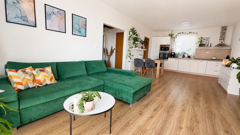 Nappali egy háromszobás lakásban kényelmes zöld kanapéval és fa dekorációjú padlóval.