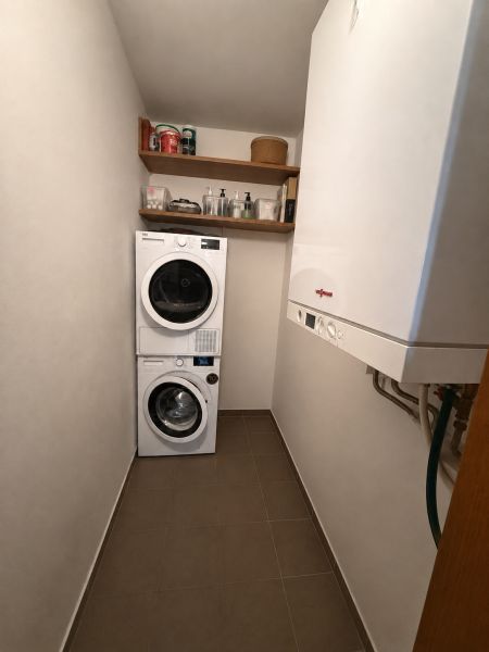 Mosókonyha egy háromszobás lakásban mosógéppel, szárítógéppel, polcokkal és gázkazánnal.