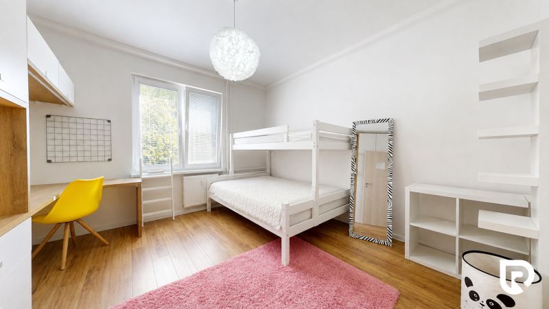 Gyerekszoba egy háromszobás lakásban emeletes ággyal, sárga székkel, polcokkal és fa dekorációjú padlóval.