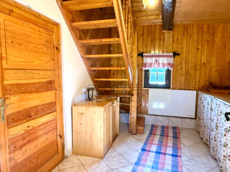 Családi ház belső tere fa lépcsővel, mennyezettel és ajtókkal, padlón csempével.