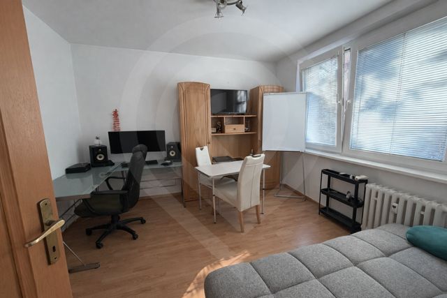 3 szobás lakás belső tere fa dekor padlóval, íróasztallal és kanapéval.