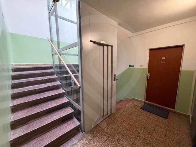 A társasházban lépcső, lift és egy háromszobás lakás ajtaja található.
