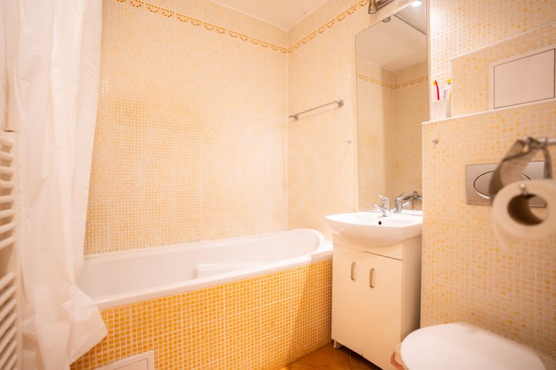 Fürdőszoba egy négy szobás lakásban káddal, mosdóval és WC-vel, világos csempékkel.