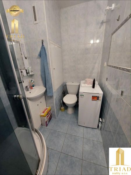 Fürdőszoba egy egyszobás lakásban kék csempével, zuhanyzóval és WC-vel.