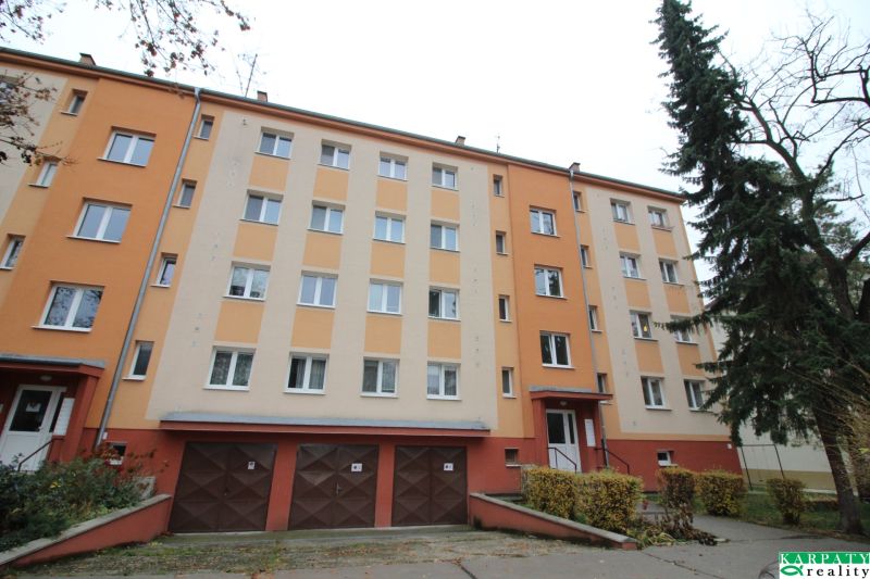 Tömbház Trnavában színes homlokzattal, garázsokkal és fákkal körülvett környezettel.