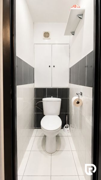 Fehér és szürke csempézett fürdőszoba, tárolóhely a WC fölött.