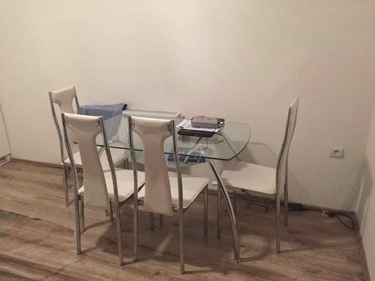 Üveg étkezőasztal fehér székekkel, fa dekor padlón.