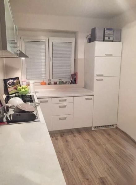 Konyha egy kétszobás lakásban fehér szekrényekkel és fa mintázatú padlóval.