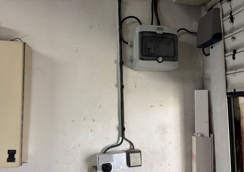 Elektromos szerelés a garázsban szekrénnyel és kábelekkel a falon.