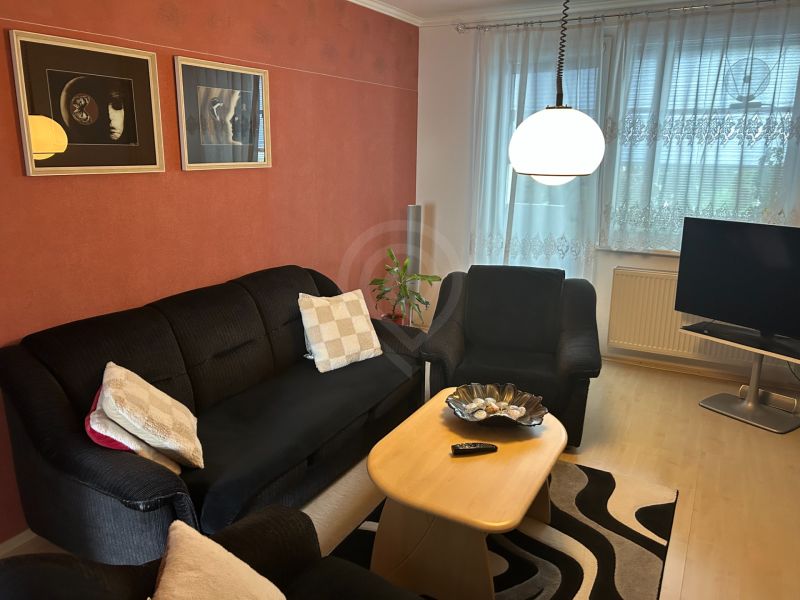 Nappali egy háromszobás lakásban kanapéval, asztallal és faldekorációkkal.