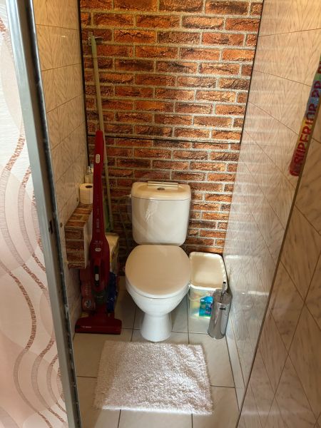 Fürdőszoba egy háromszobás lakásban WC-vel, téglamintával és tisztítószerekkel.
