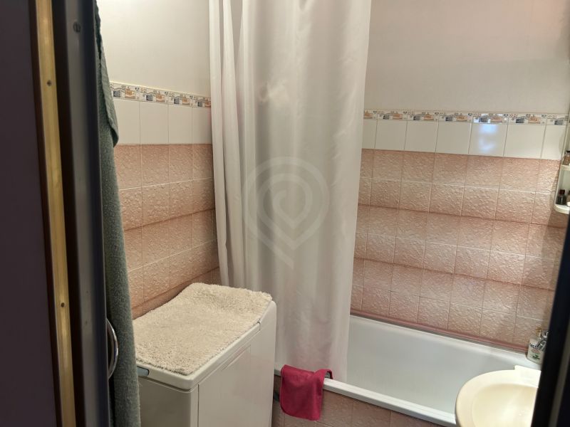Fürdőszoba káddal, mosógép törölközővel és csempékkel egy háromszobás lakásban.