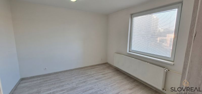 Szoba egy kétszobás lakásban fehér falakkal és fa dekorációjú padlóval.