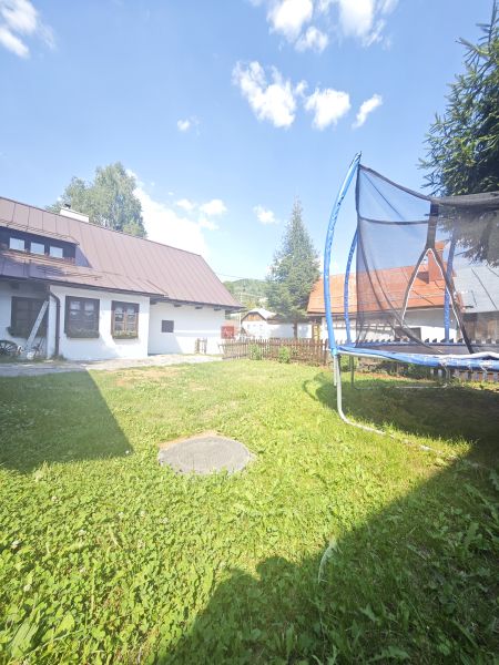 Házikó Špania Dolinában, trambulin a füves kertben a kék ég alatt.
