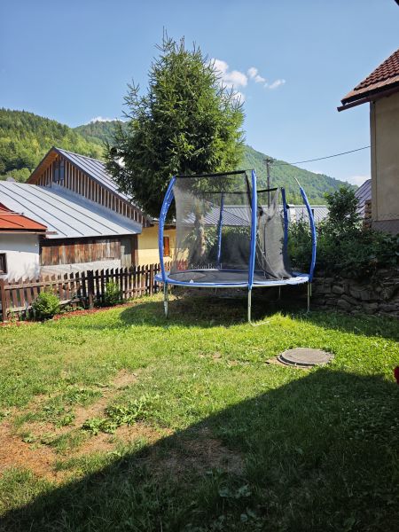 Trambulin a ház mellett a Špania Dolinán, körülötte fű és fák a háttérben.