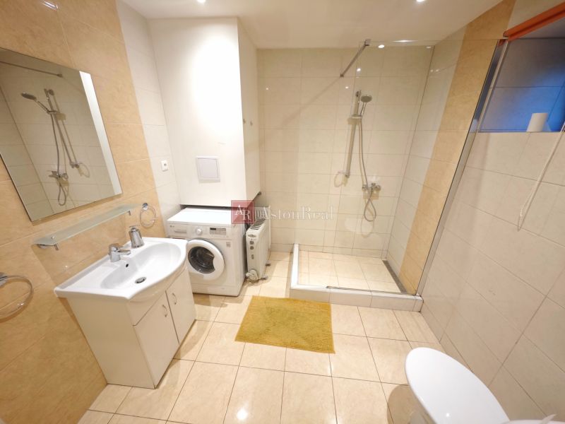 Fürdőszoba a házikóban mosógéppel, zuhanyzóval és fa dekoros padlóval.