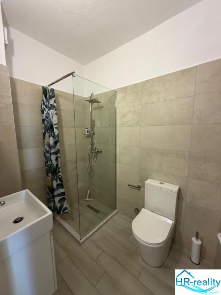 Fürdőszoba garzonlakásban WC-vel, zuhanyzóval és mosdóval.