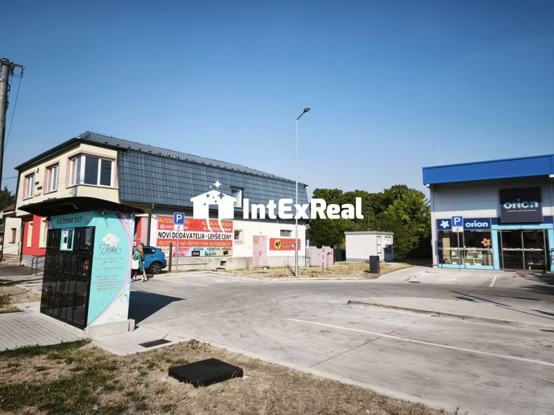 Üzlethelyiségek az SNP utcában, Šaľa városában, parkolóval és reklámfeliratokkal.