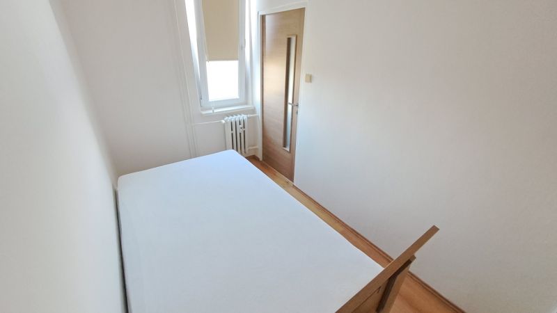 Hálószoba fehér falakkal és fa dekorációjú padlóval egy kétszobás lakásban.