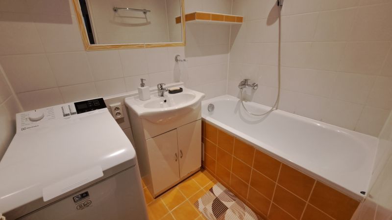 Fürdőszoba egy kétszobás lakásban zuhanyzóval, mosógéppel és mosdóval.