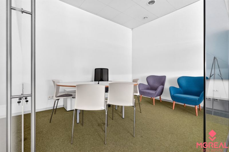 Irodai helyiség konferenciaasztallal, színes fotelekkel és egyszerű székekkel.