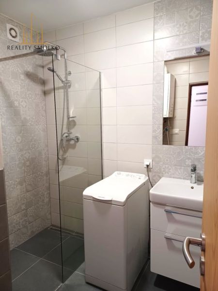 Fürdőszoba egy kétszobás lakásban mosógéppel, zuhanyzóval és mosdóval.