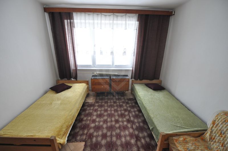 Hálószoba két egyszemélyes ággyal, szőnyeggel és ablakkal egy kétszobás lakásban.