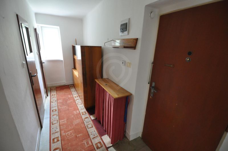 Keskeny folyosó szőnyeggel és egyszerű bútorokkal egy kétszobás lakásban.