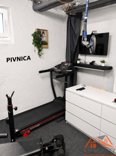 Fitnesz sarok futópaddal, televízióval és súlyzópadokkal egy háromszobás lakás pincéjében.