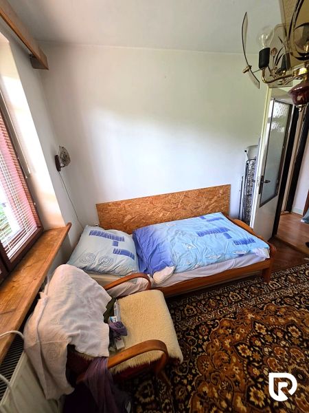 Szoba egy családi házban régi szőnyeggel, székkel és ággyal az ablak mellett.