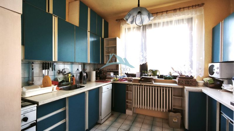 Családi ház konyhája kék konyhabútorral és nagy ablakkal, otthonos légkör.